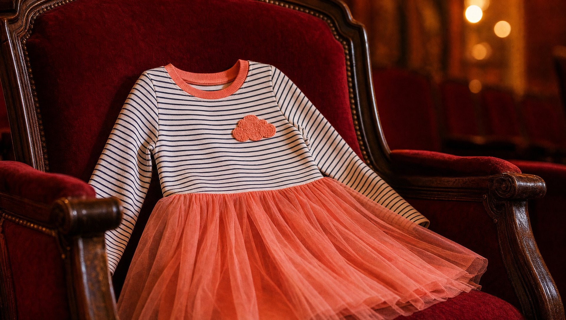 Striped long sleeve kids dress with a peachy pink skirt on a red velvet theater seat