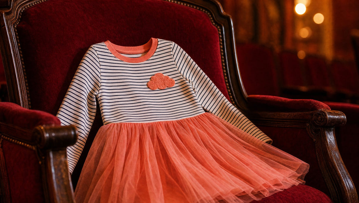 Striped long sleeve kids dress with a peachy pink skirt on a red velvet theater seat