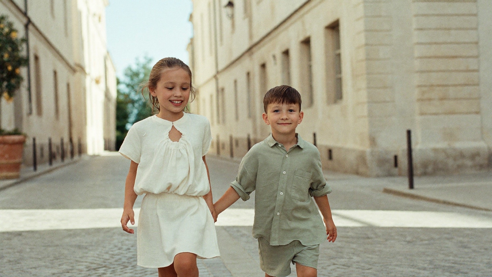 Girl and boy in linen summer outfits walking on an old European street