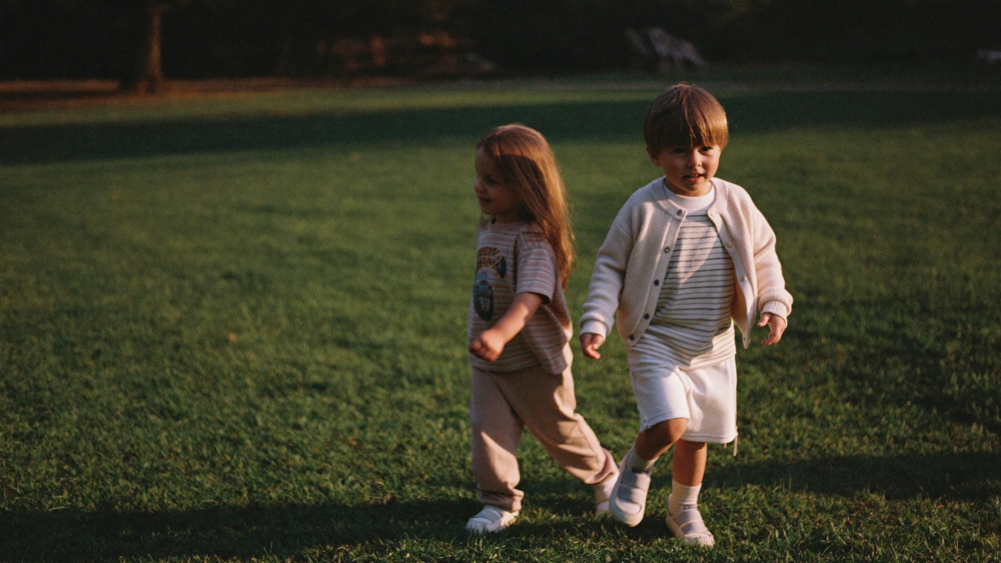 Two young children walking on grass in summer cotton clothing